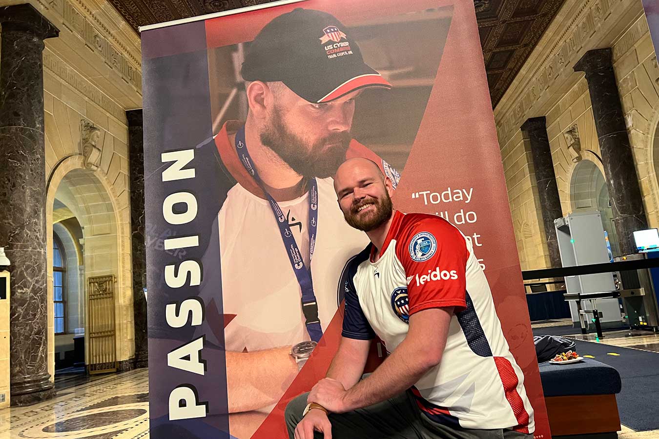 Logan Stratton pictured in front of a US Cyber poster featuring himself. 