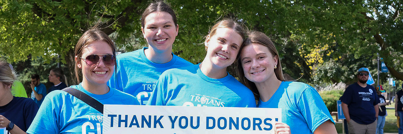 DSU volleyball players hold a thank you donor signs during Trojans Give Back 2024.