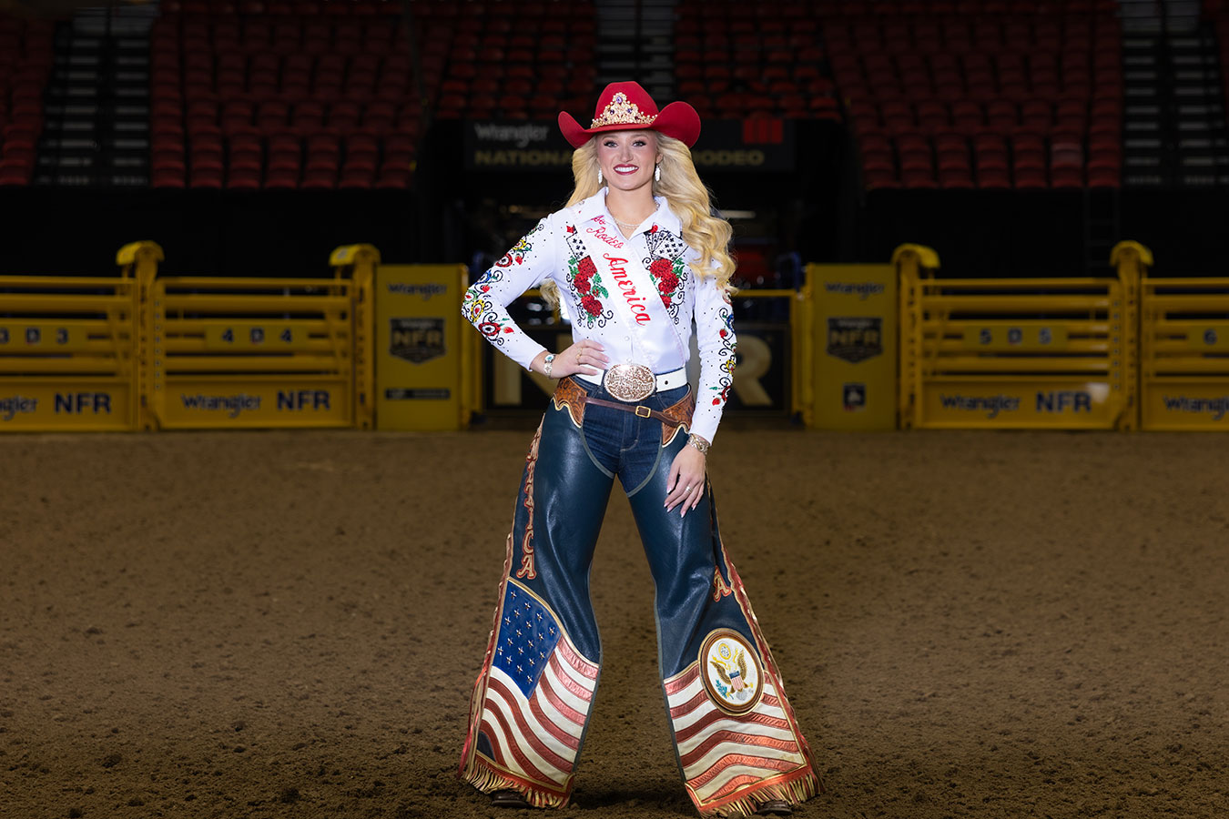 Callie Mueller is Miss Rodeo America pictured in an arena wearing her chaps, a sash, and hat. Photo credit to Sherry Smith Photography.